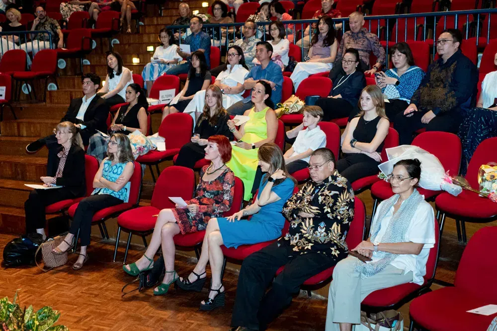A large group of people are sitting in red chairs in an auditorium.