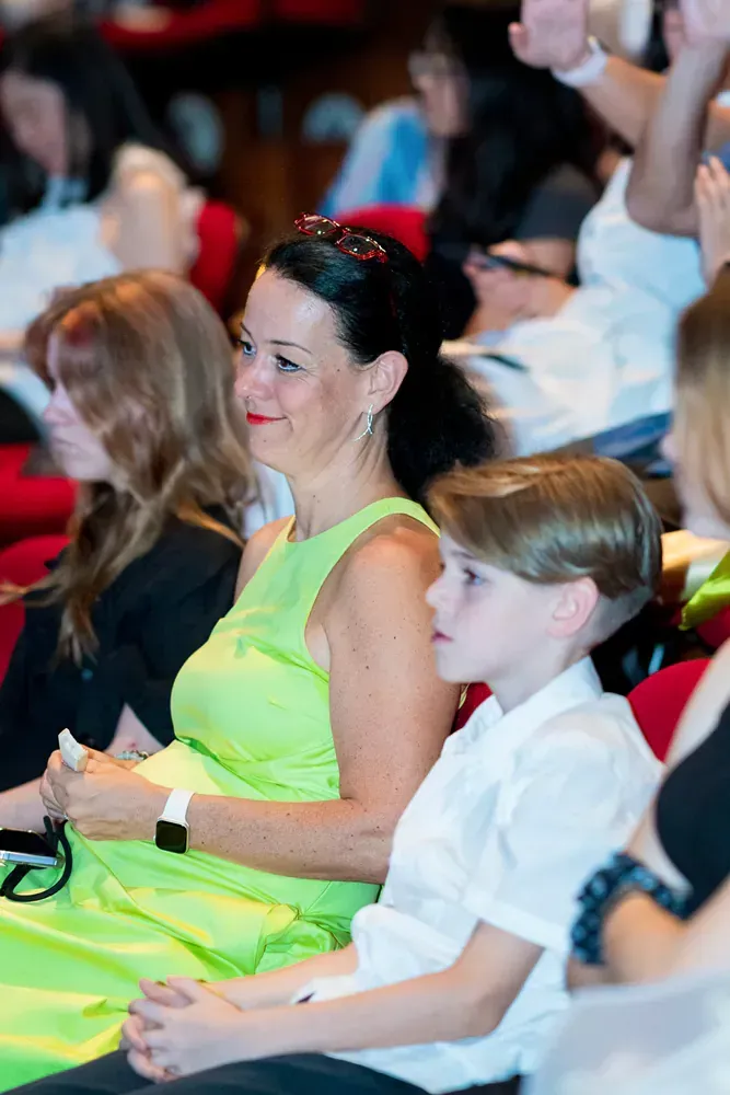 A woman in a green dress is sitting next to a boy in a crowd of people.