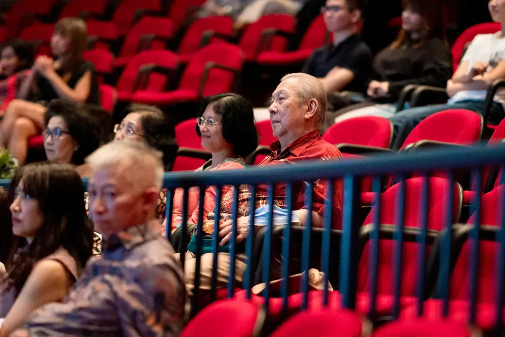 A group of people are sitting in red chairs in an auditorium.