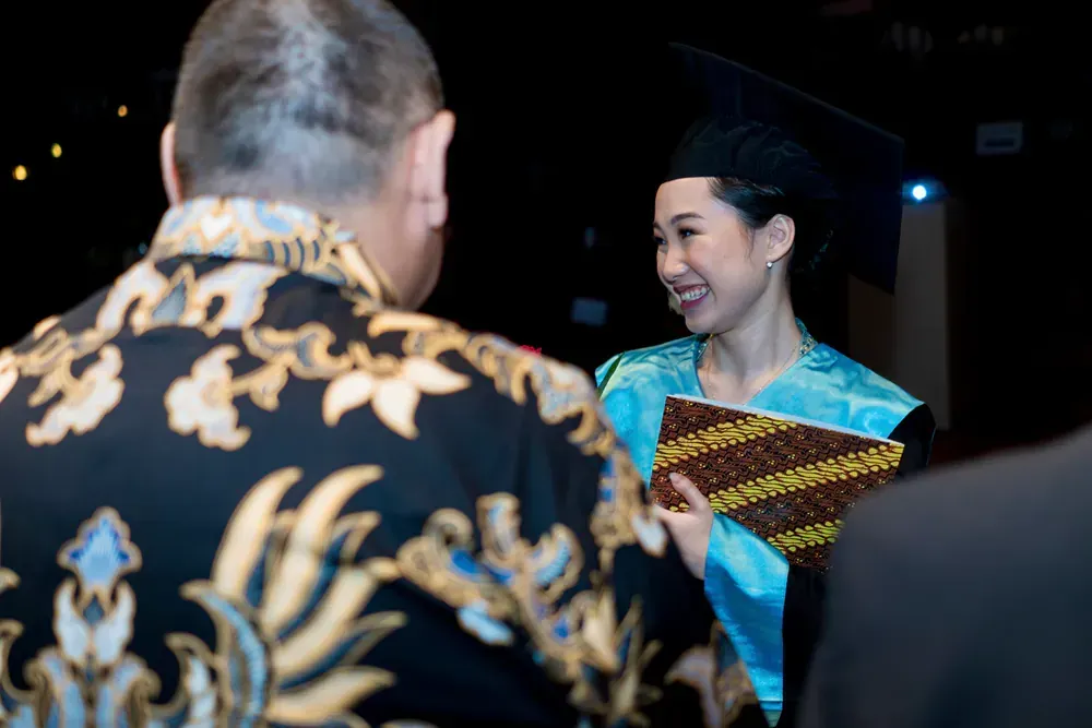 A woman in a graduation cap and gown is talking to a man in a black shirt.