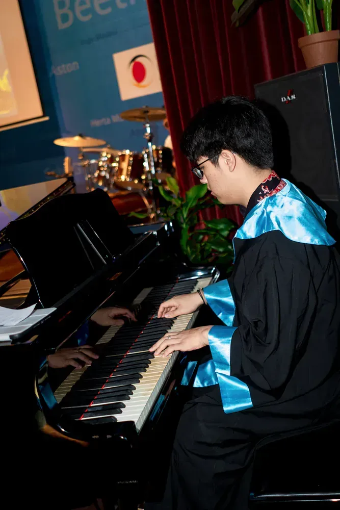 A man in a graduation gown is playing a piano
