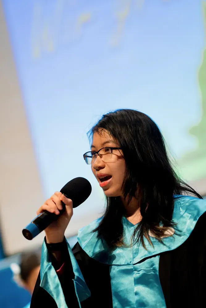 A woman in a graduation gown is singing into a microphone.