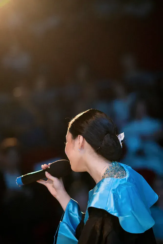 A woman in a graduation cap and gown is singing into a microphone.