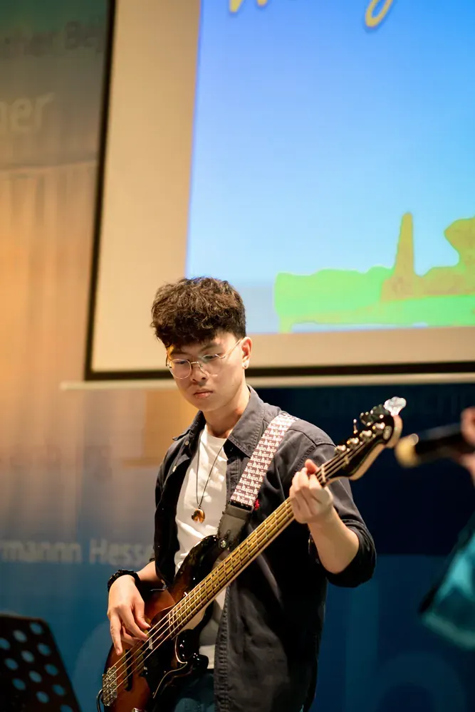 A young man is playing a bass guitar in front of a projector screen.