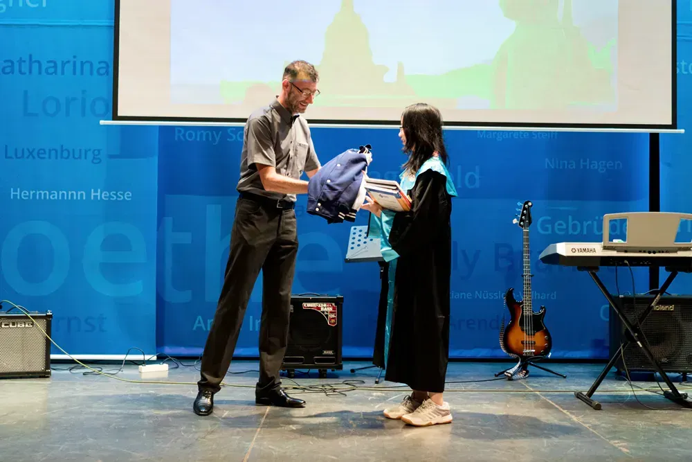 A man is giving a backpack to a woman on a stage.