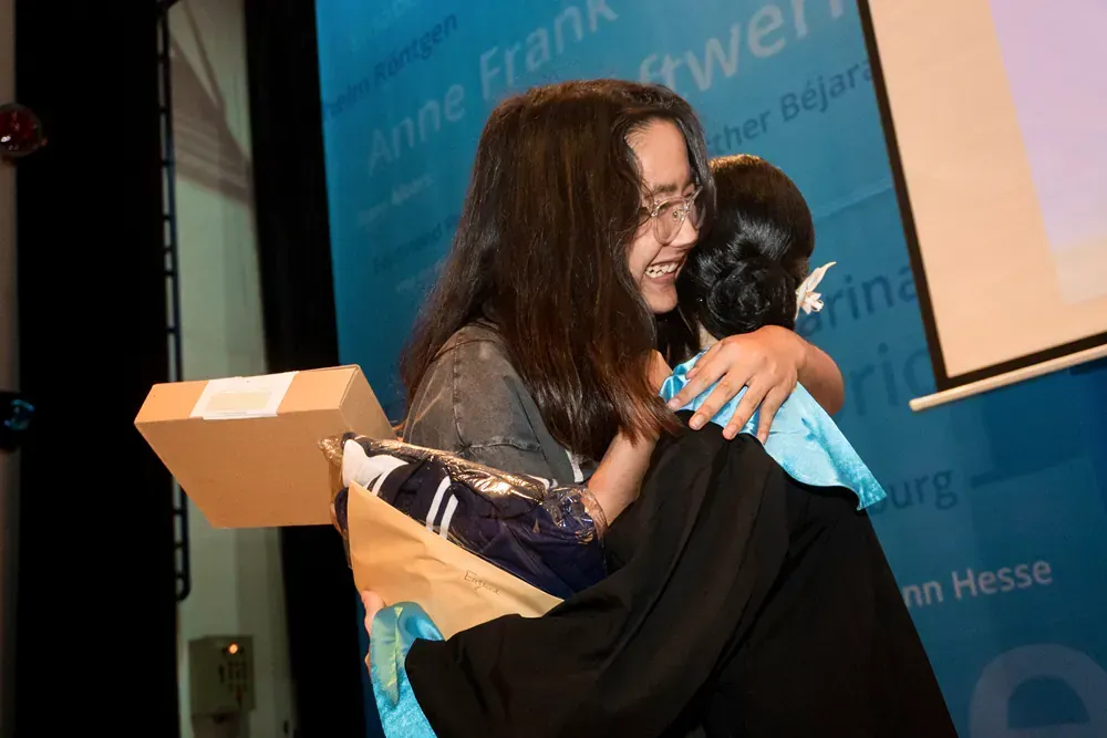 A woman is hugging another woman in front of a projector screen.