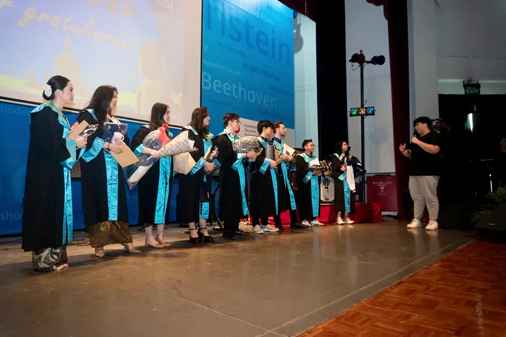 A group of people are standing on a stage holding flowers.