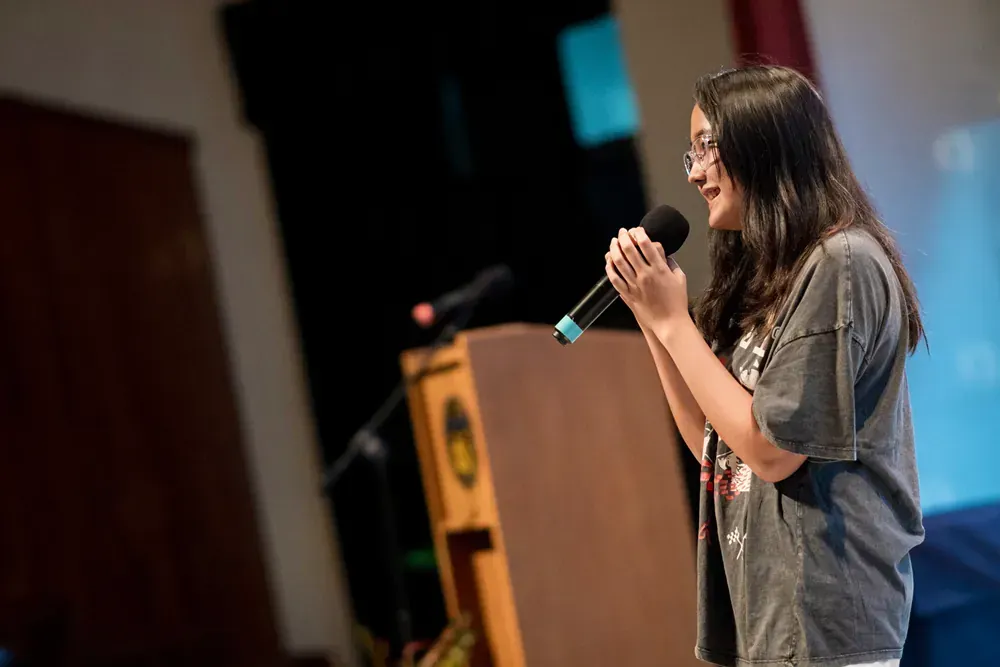 A young woman is standing at a podium holding a microphone.