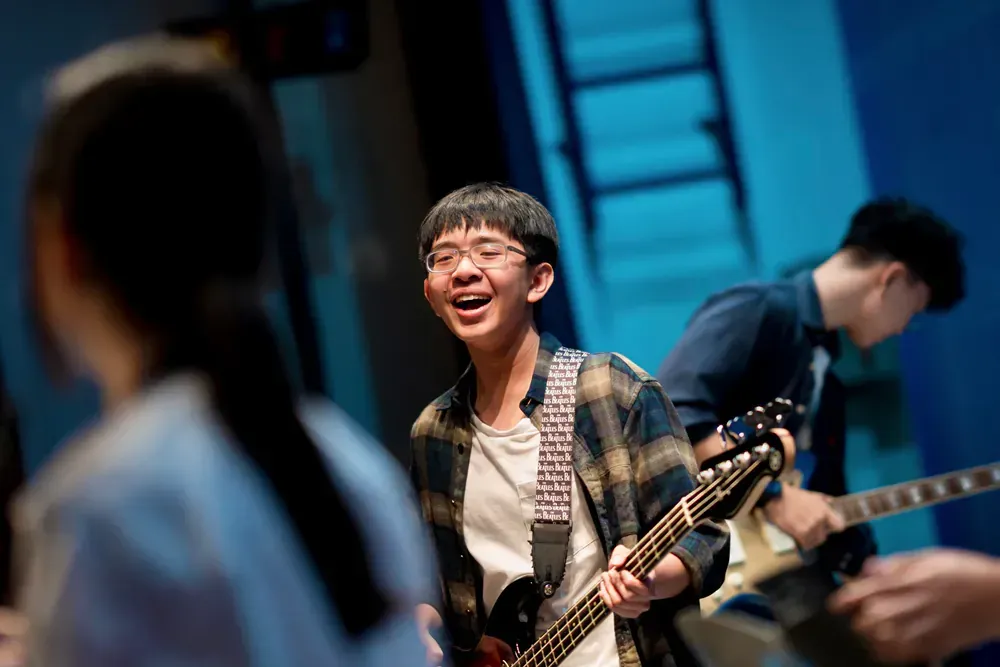 A young man is playing a guitar in a band on a stage.
