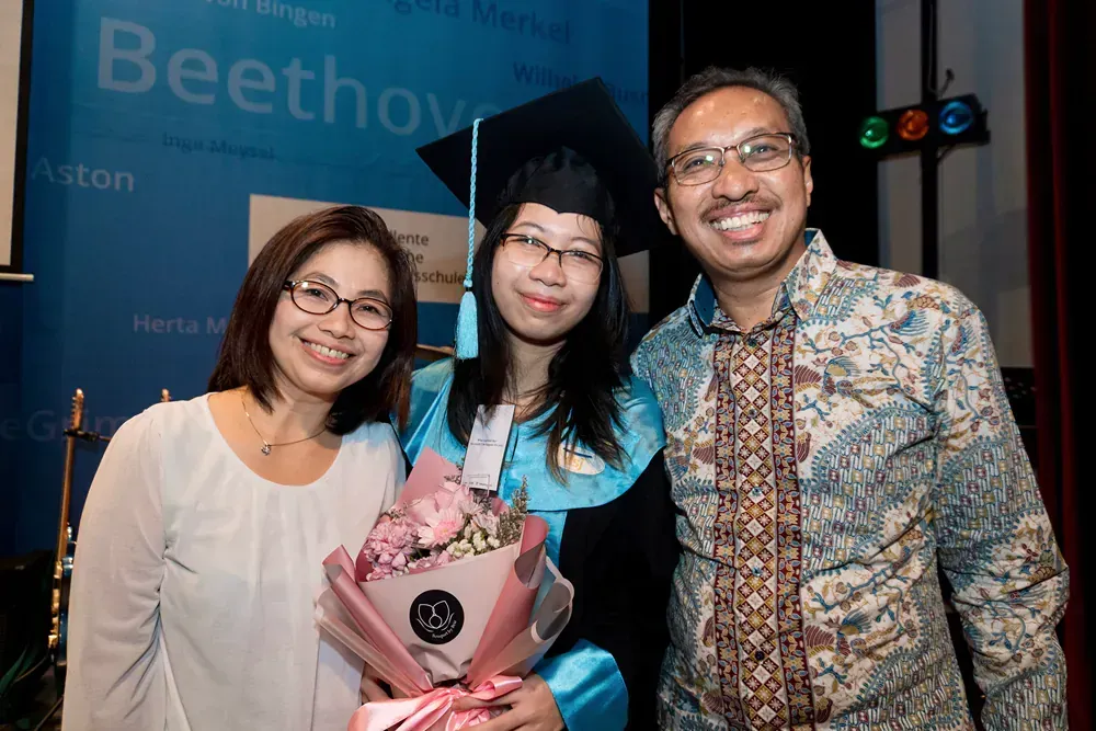 A woman in a graduation cap and gown is posing for a picture with her parents.