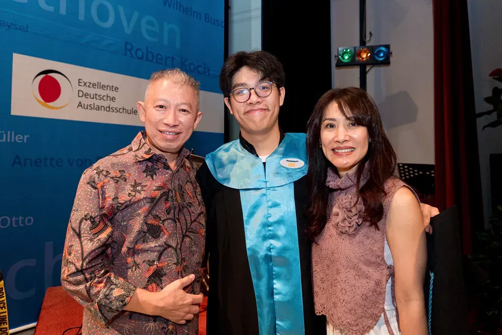 A man in a graduation cap and gown is posing for a picture with two other people.