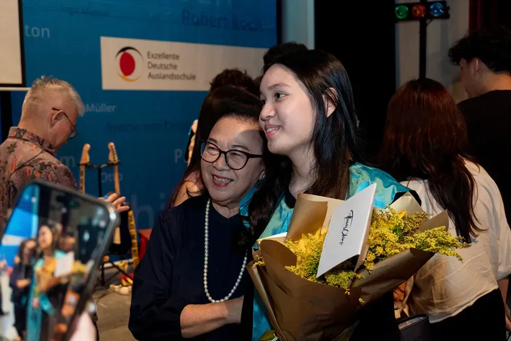 Two women are posing for a picture with a bouquet of flowers.