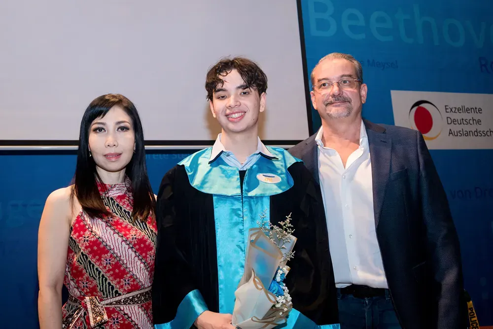 A man and woman are standing next to a young man in a graduation gown