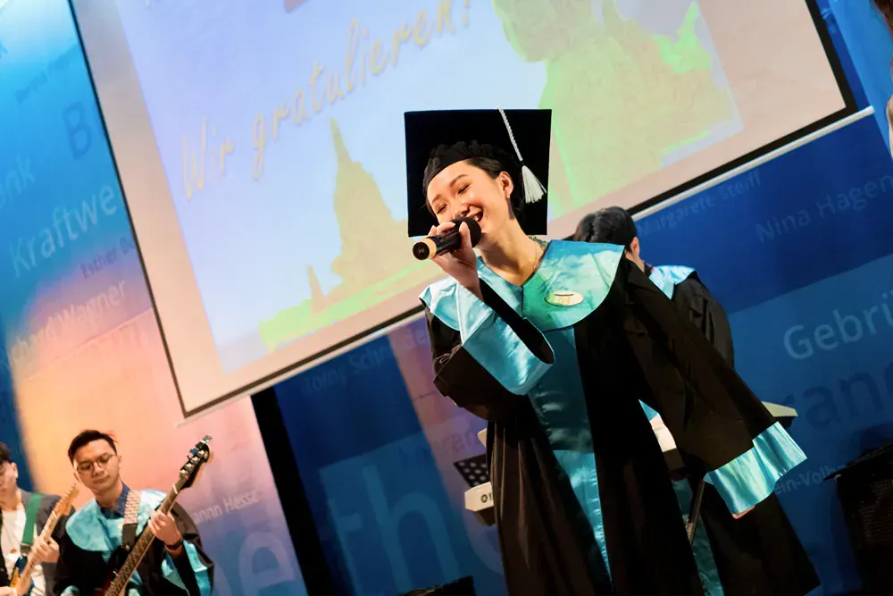 A woman in a graduation cap and gown is singing into a microphone.