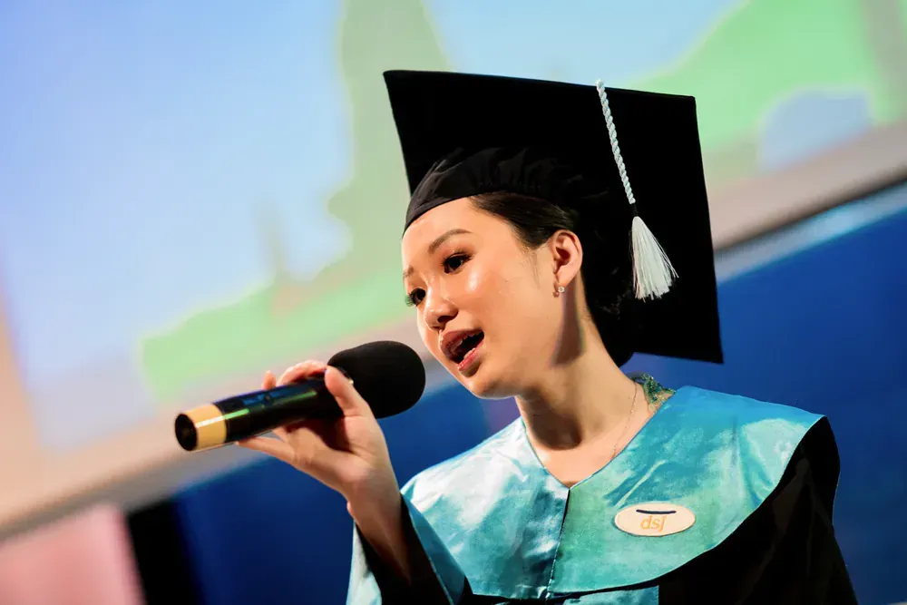 A woman in a graduation cap and gown is singing into a microphone.