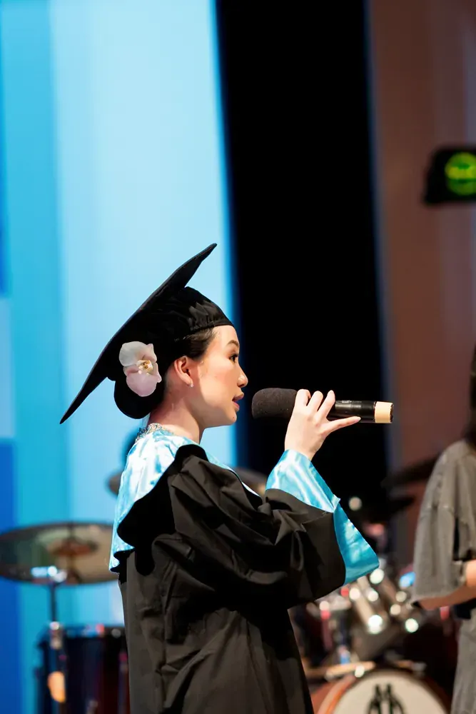 A woman in a graduation cap and gown is singing into a microphone