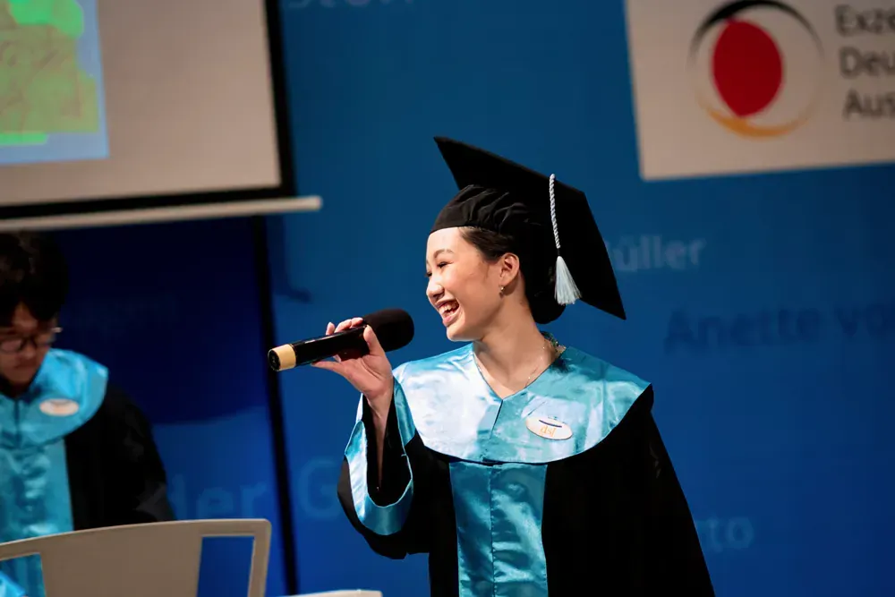 A woman in a graduation cap and gown is singing into a microphone
