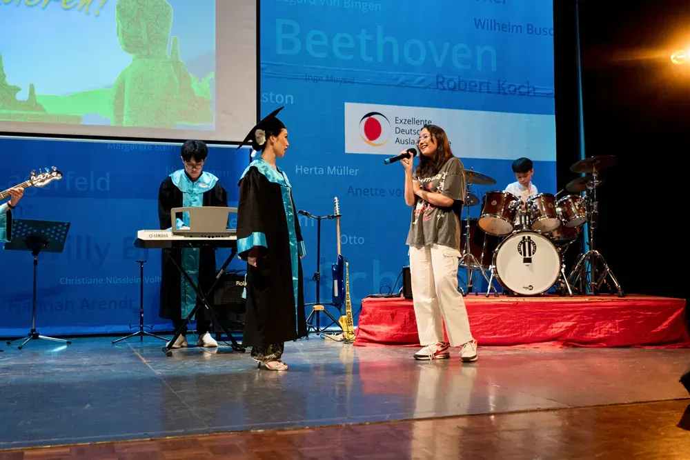A woman in a graduation cap and gown is singing into a microphone on a stage.