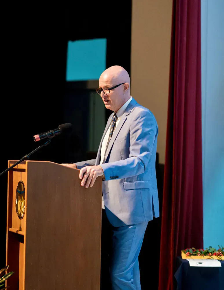 A man in a suit and tie is standing at a podium speaking into a microphone.