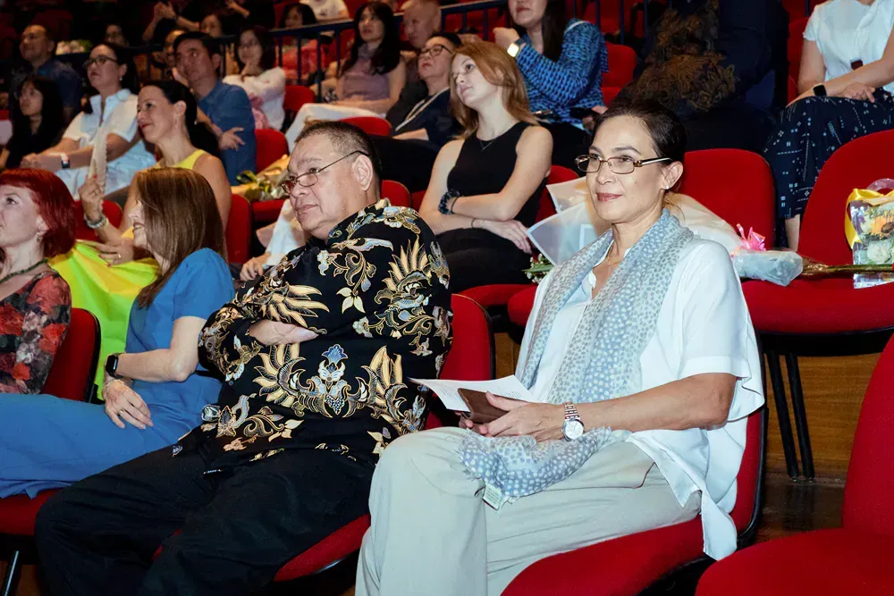 A group of people are sitting in red chairs watching a presentation