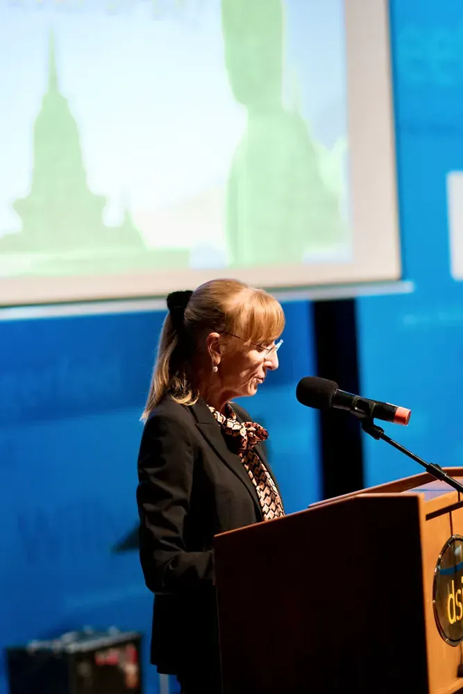 A woman is standing at a podium speaking into a microphone.