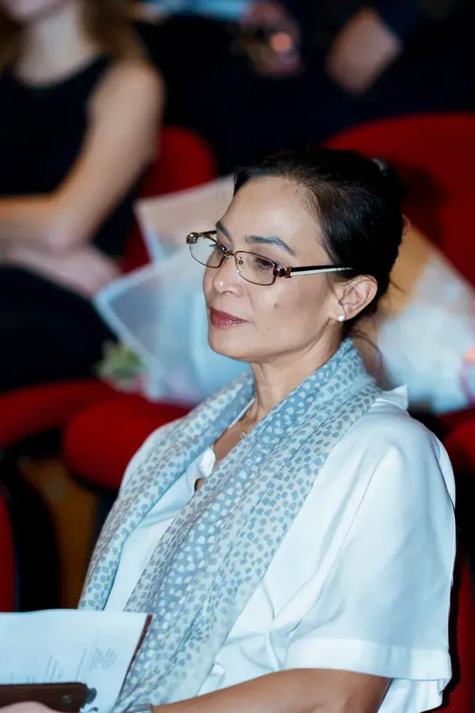 A woman wearing glasses and a scarf is sitting in a theatre.