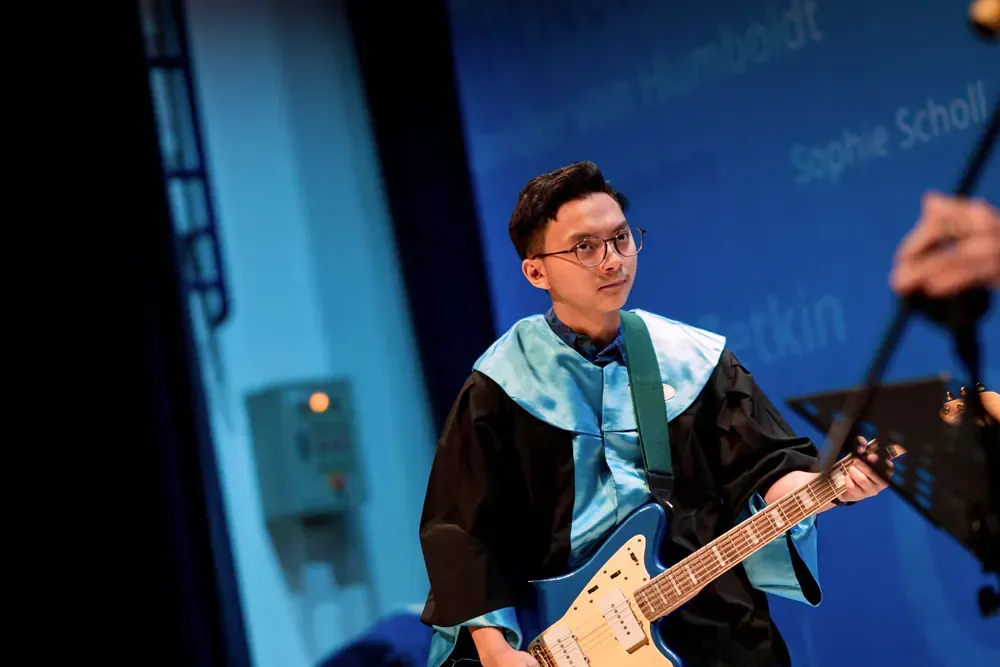 A man in a graduation gown is playing a guitar