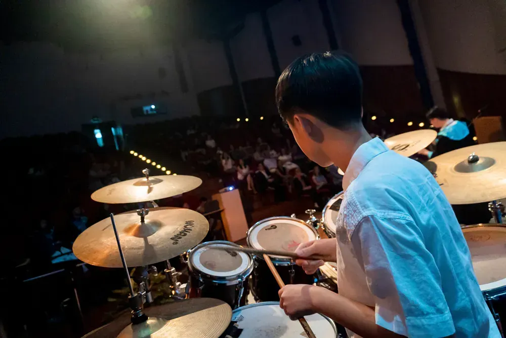A young boy is playing drums on a stage in front of a crowd.