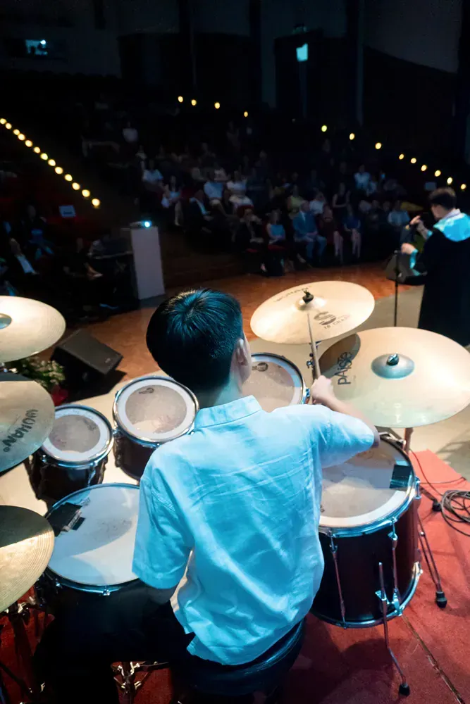 A man is playing drums on a stage in front of a crowd.