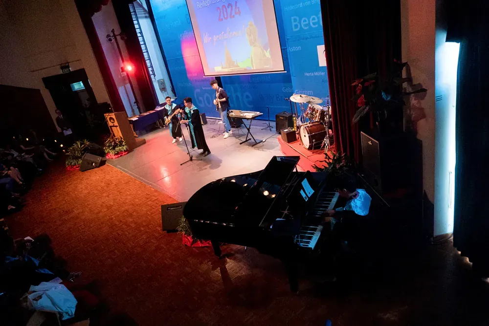 A group of people are playing instruments on a stage in front of a projector screen.