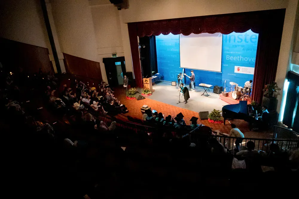 A group of people are sitting in an auditorium in front of a stage.