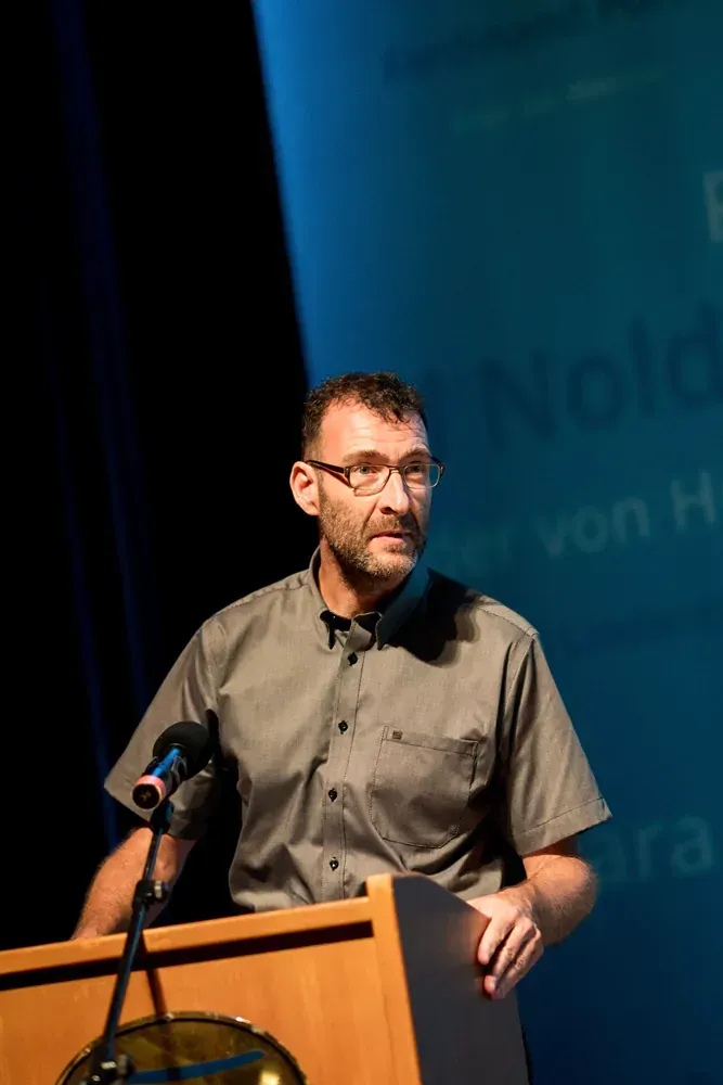 A man is standing at a podium speaking into a microphone.