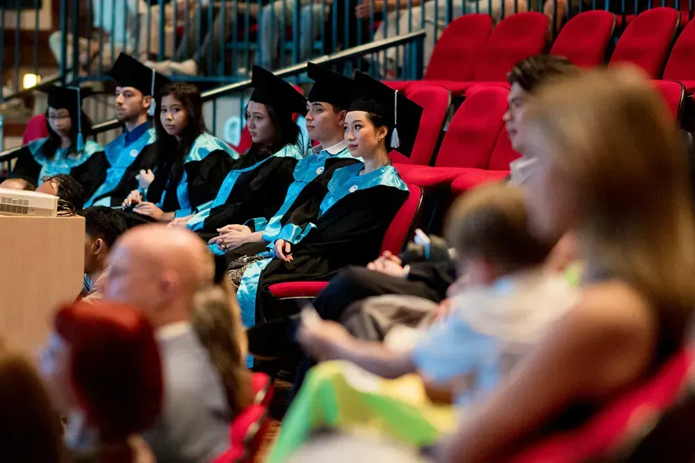A group of graduates are sitting in red chairs at a graduation ceremony.