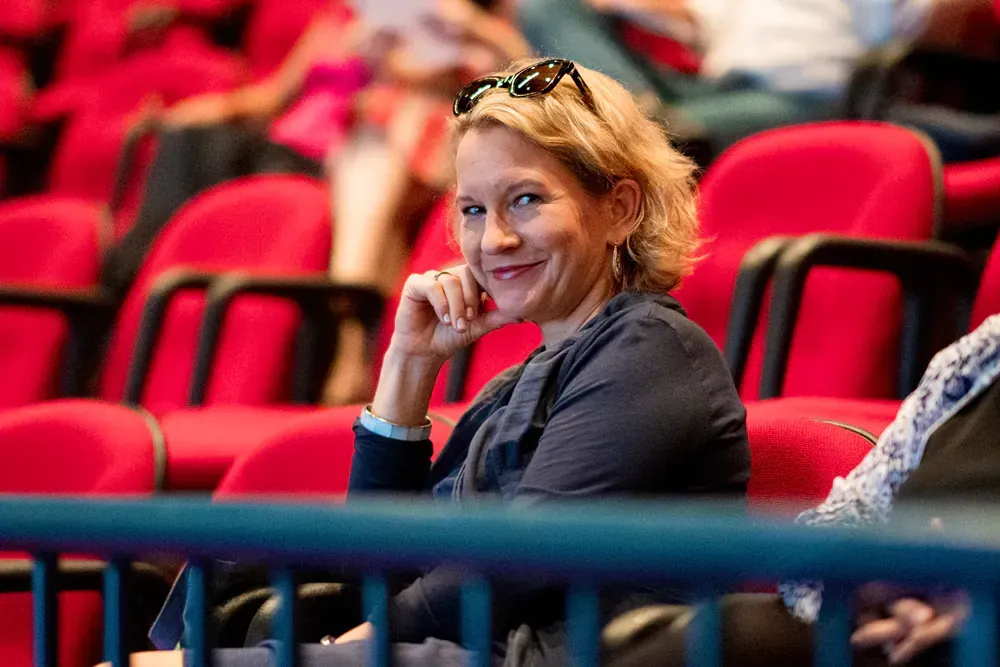 A woman is sitting in a stadium watching a game and smiling.