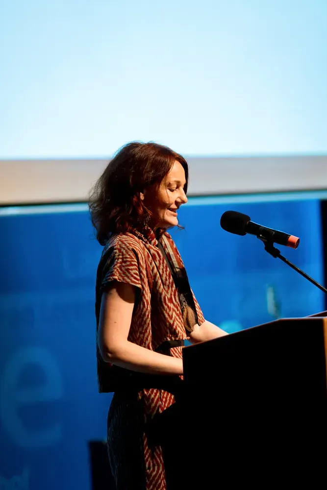 A woman stands at a podium speaking into a microphone