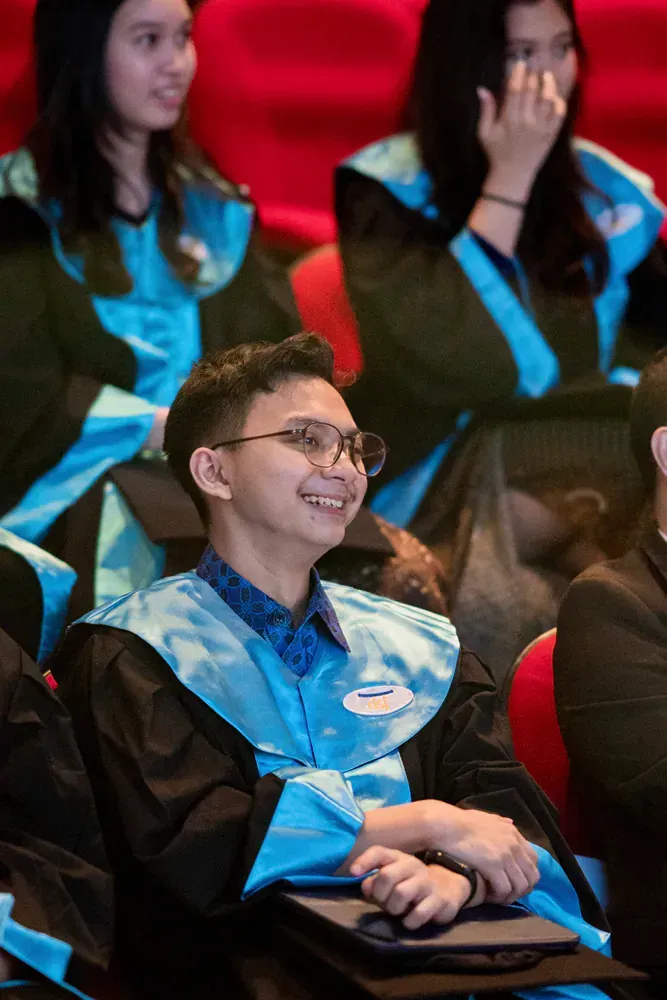 A group of graduates are sitting in a auditorium and smiling.