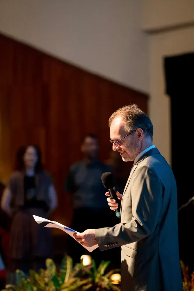 A man in a suit is holding a microphone and reading a piece of paper