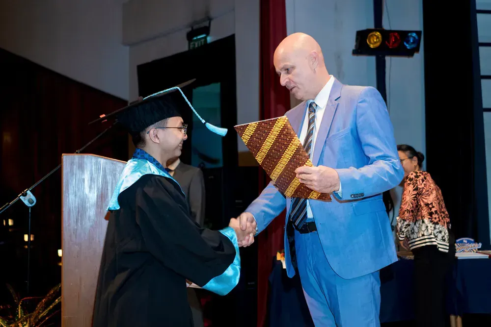 A man in a suit is shaking hands with a man in a graduation cap and gown.