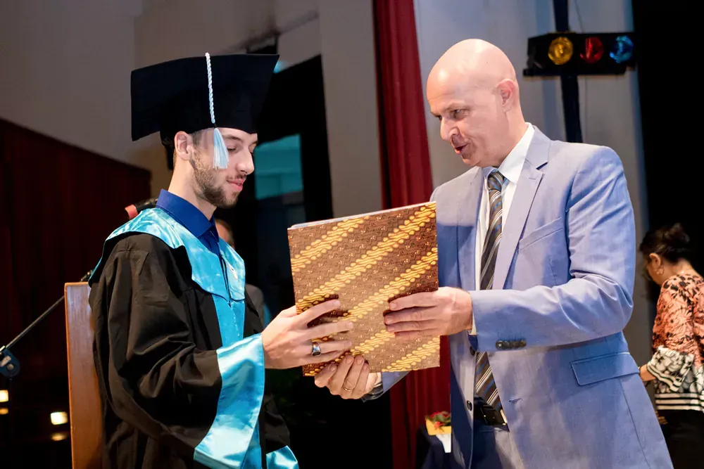 A man in a suit is giving a diploma to a man in a graduation cap and gown.