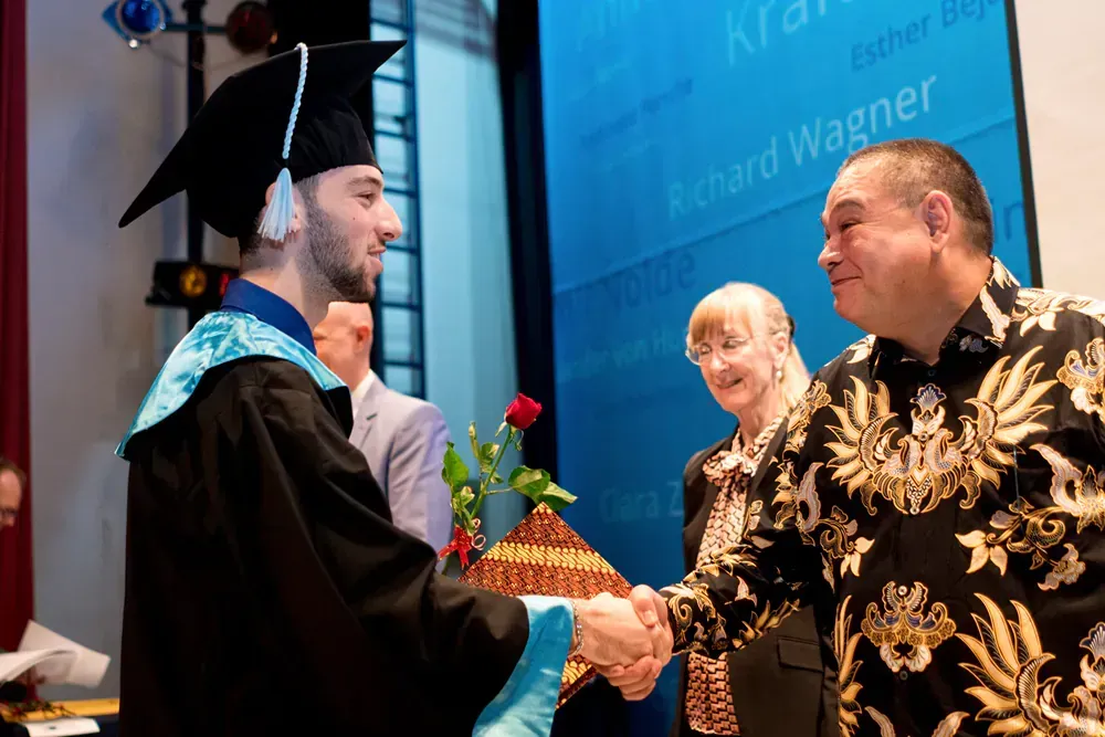 A man in a graduation cap and gown is shaking hands with a man in a floral shirt.