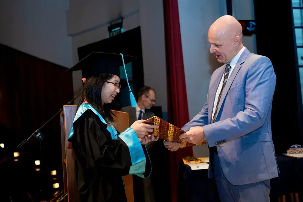 A man in a suit is giving a gift to a woman in a graduation cap and gown.