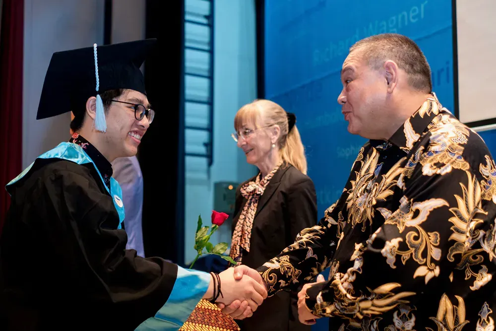A man in a graduation cap and gown is shaking hands with another man.