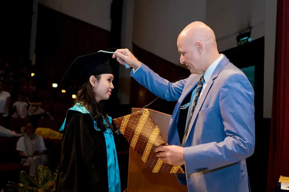 A man in a suit is putting a ribbon on a graduate 's cap