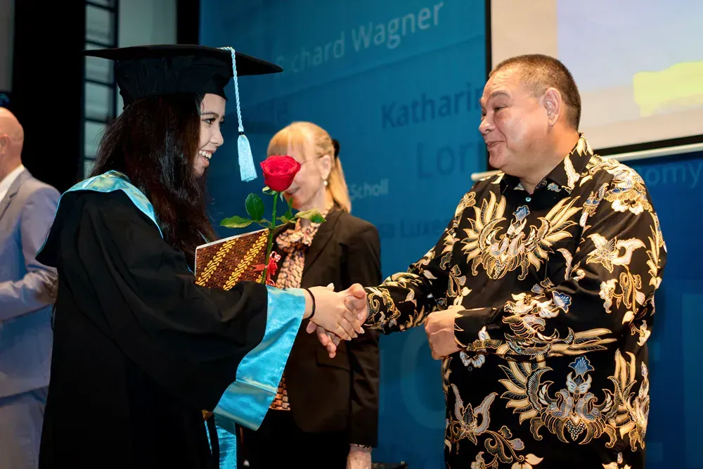 A woman in a graduation cap and gown shakes hands with a man