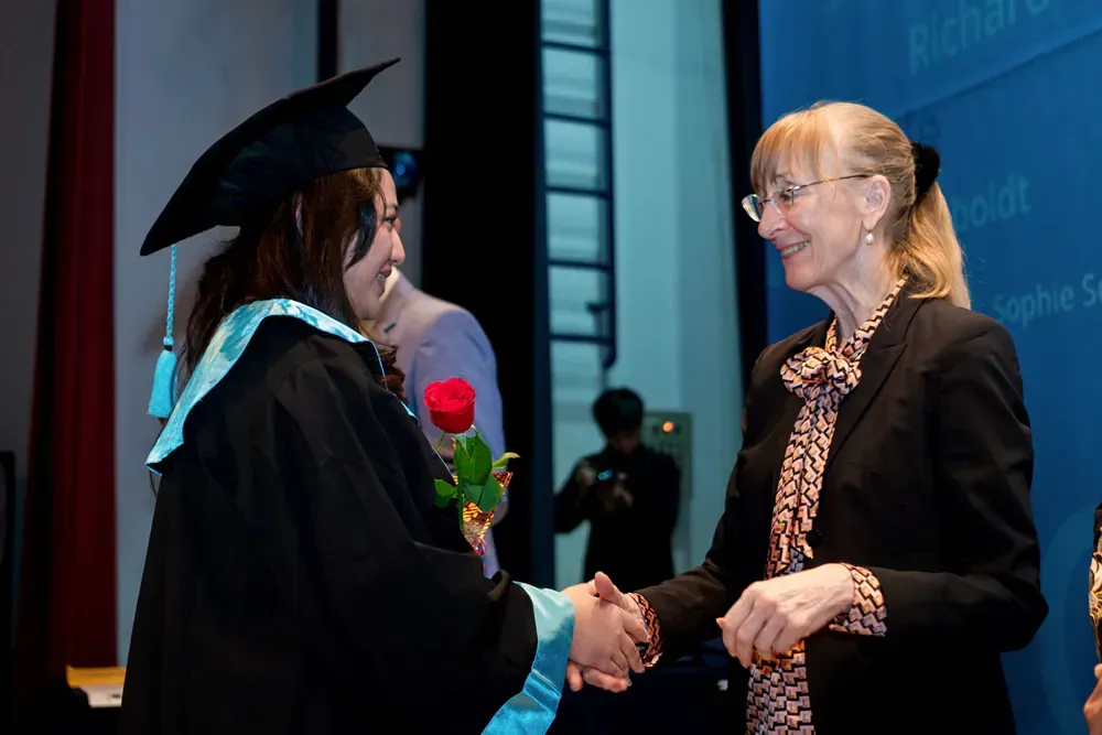 A woman in a graduation cap and gown is shaking hands with another woman