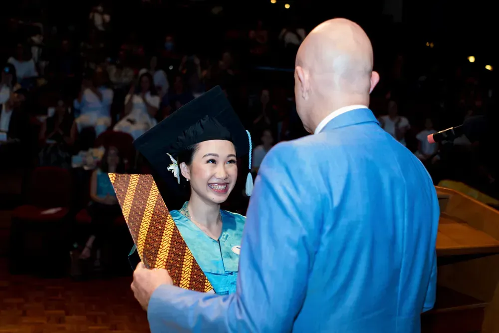 A man in a blue suit is giving a diploma to a woman in a graduation cap and gown.