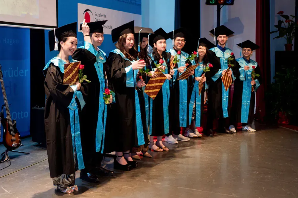 A group of graduates are standing on a stage holding flowers.