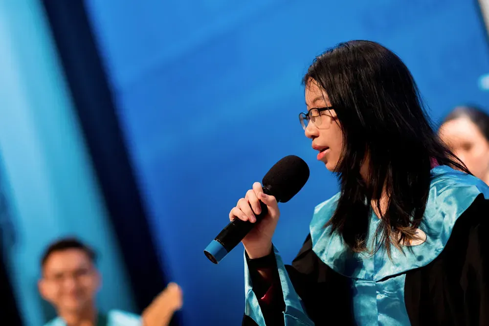 A woman in a graduation gown is singing into a microphone