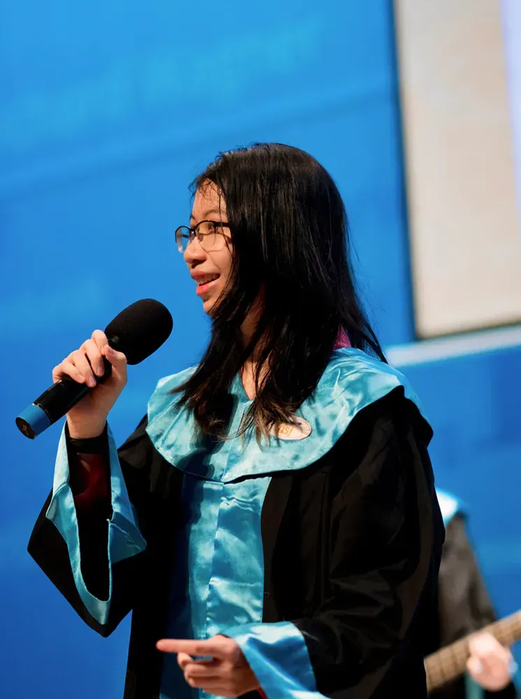 A woman in a graduation gown is singing into a microphone