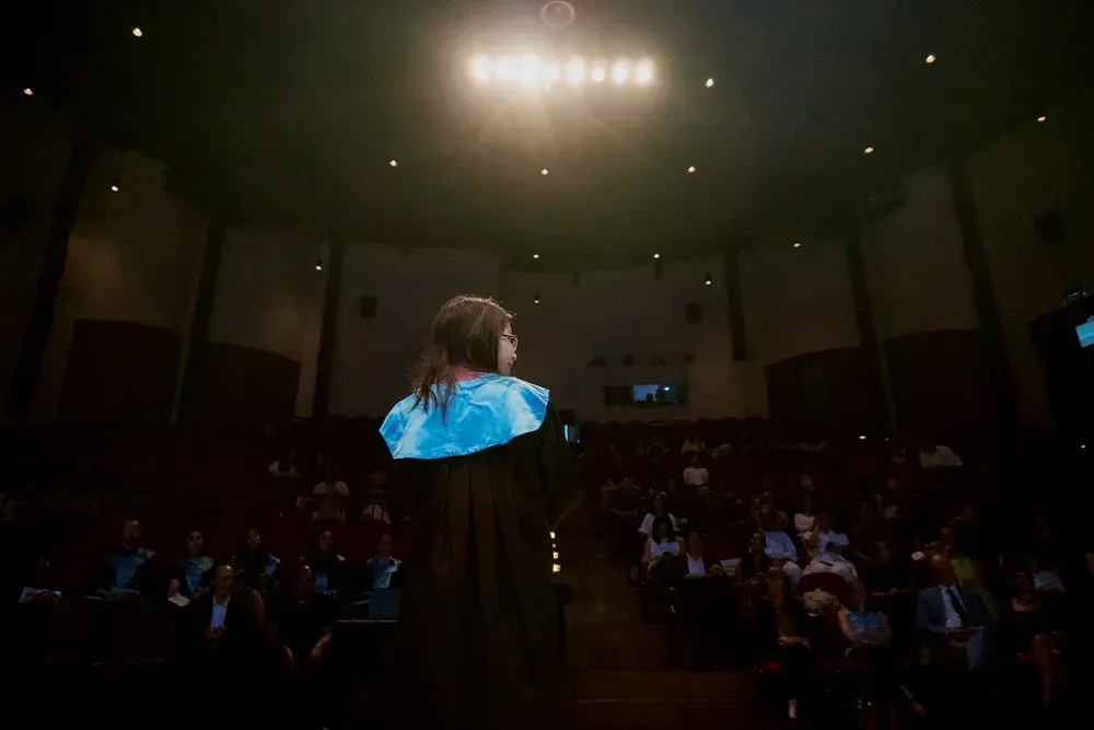 A woman in a graduation cap and gown is standing in front of a crowd in an auditorium.